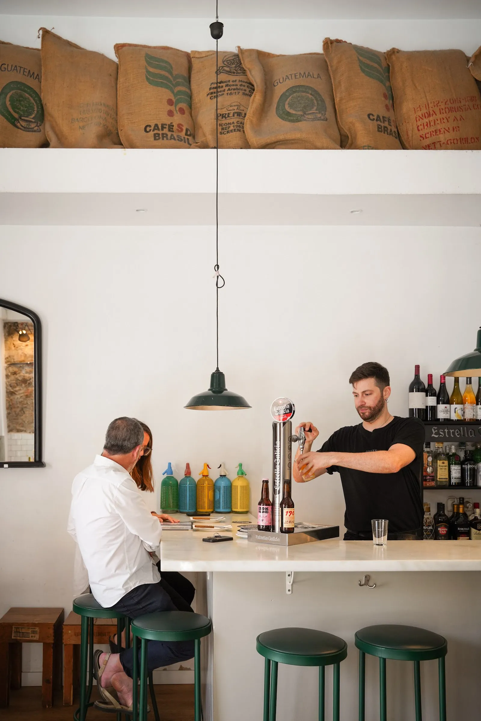 La barra con taburetes verdes y sacos de café